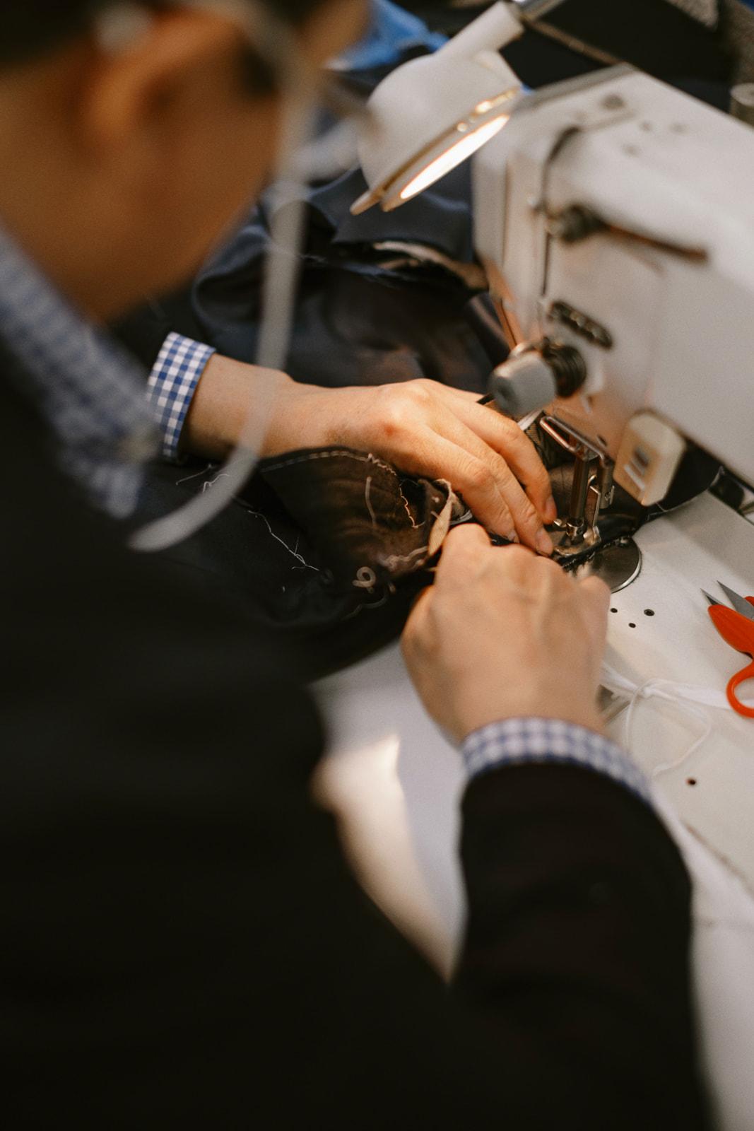 A tailor's hands guiding fabric through a sewing machine at the factory