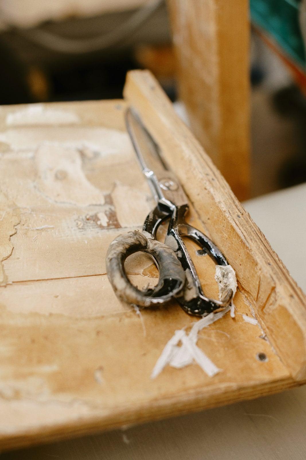 Vintage tailor's shears resting on a chalk-marked wooden cutting board at the factory